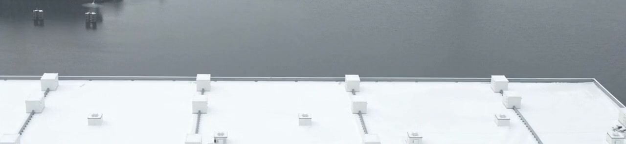 The white roof of a cold store from above, its roof units in rows, with open water beyond